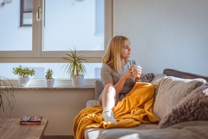Une femme chez elle, une tasse à la main, près de la fenêtre